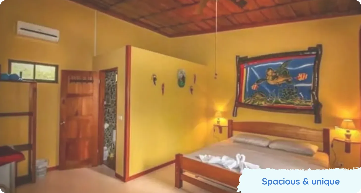 Bedroom with yellow walls, wooden furniture, wall art and towel animals on the bed. Text reads Spacious & unique.